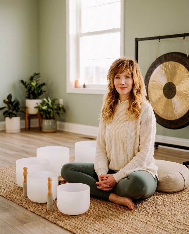 Kara Looney seated with crystal singing bowls and a gong in a serene wellness studio, Founder & CEO of Coliberation Wellness